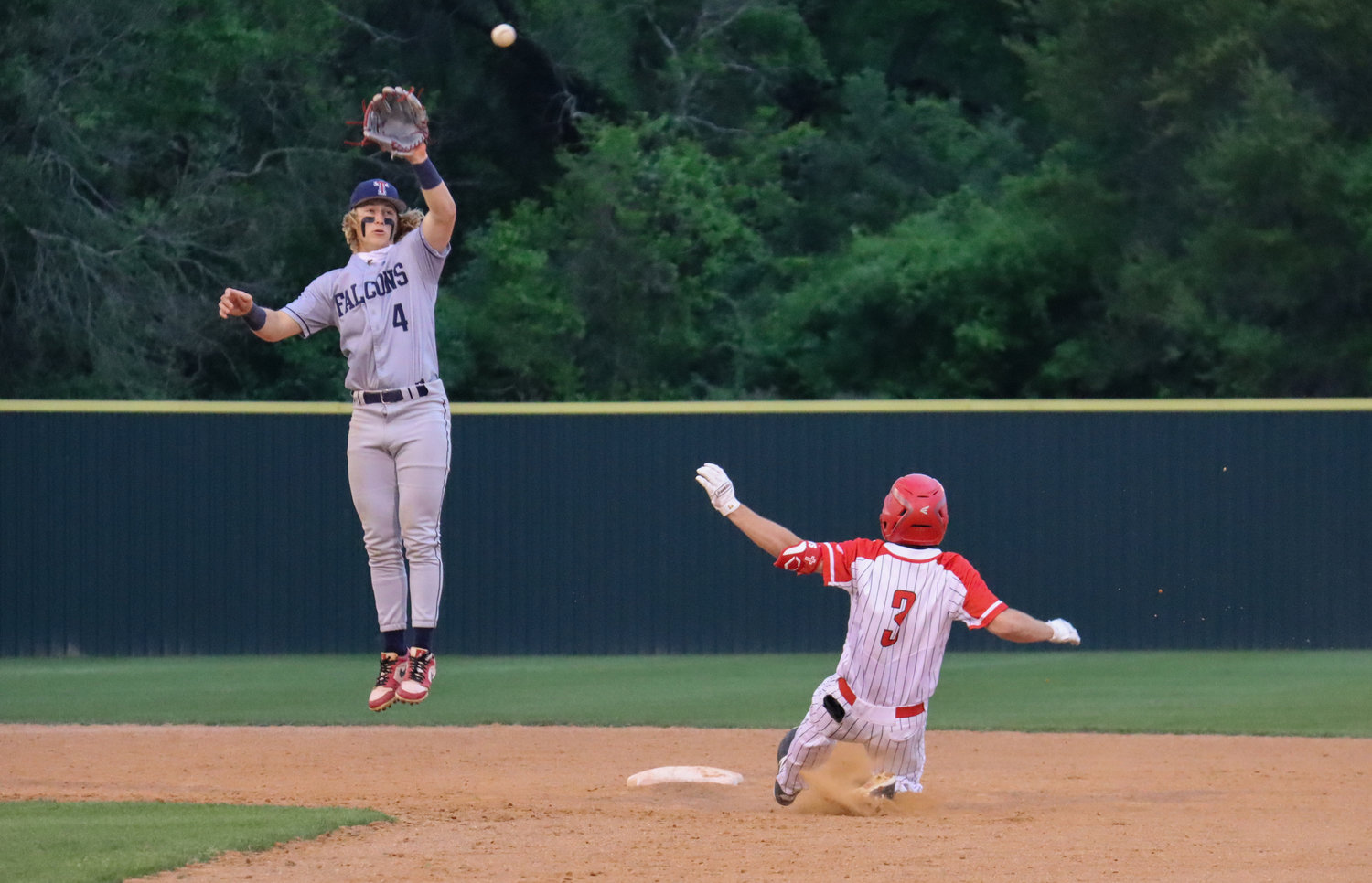 Tompkins senior first baseman Will Stark (4) leaps in an attempt to catch a wayward throw as Katy senior Caleb Matthews (3) slides safely to second base during their game Tuesday, March 30, at Katy High.